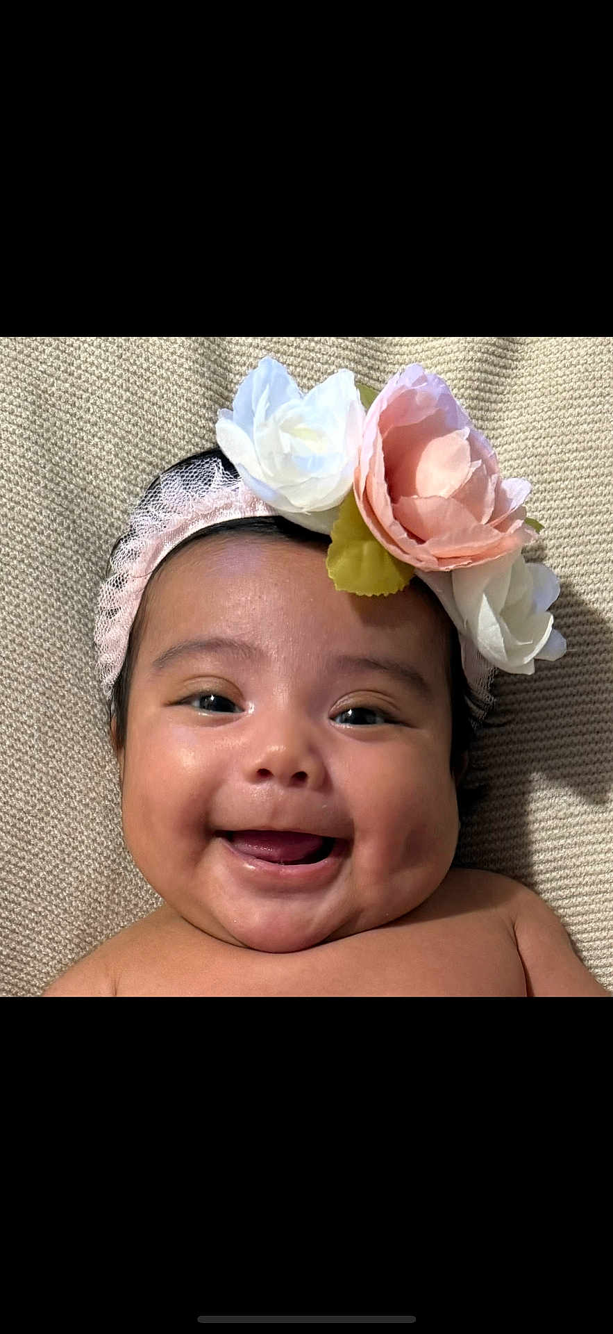 Liana is registered to the contest to win money with this photo: baby, child, smiling, face, headband, flower, cheeks, skin, portrait, closeup, happy, infant, head, cute, lying_down, texture, blanket, warm, soft, indoors