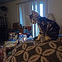 animal, blanket, bottle, box, cat, couch, curious, domestic, furniture, household_items, indoor, kitten, lamp, living_room, pattern, pet, tabby, table, vertical_blinds, window