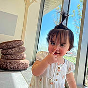 Alice is registered to the contest to win money with this photo: toddler, child, cute, indoors, window, sunlight, hair_ponytail, playful, nose_picking, white_outfit, floral_pattern, cushions, stacked_cushions, floor, hand, smile, face, person, young_child, bright