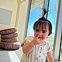 toddler, child, cute, indoors, window, sunlight, hair_ponytail, playful, nose_picking, white_outfit, floral_pattern, cushions, stacked_cushions, floor, hand, smile, face, person, young_child, bright