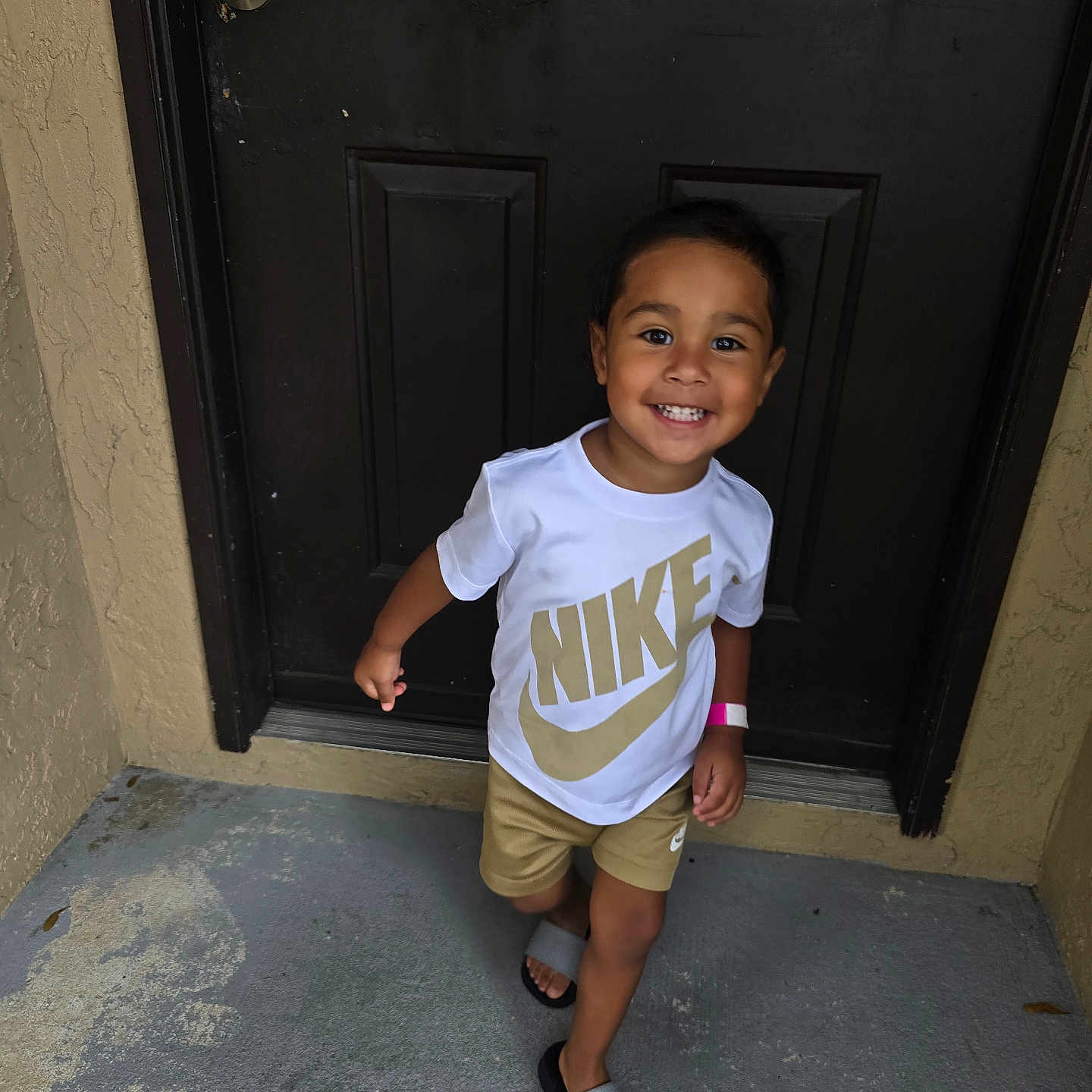 Adriel is registered to the contest to win money with this photo: casual, child, clothing, concrete, cute, door, face, footwear, happy, nike, outdoor, person, sandals, shorts, skin, smile, toddler, tshirt, walking, young