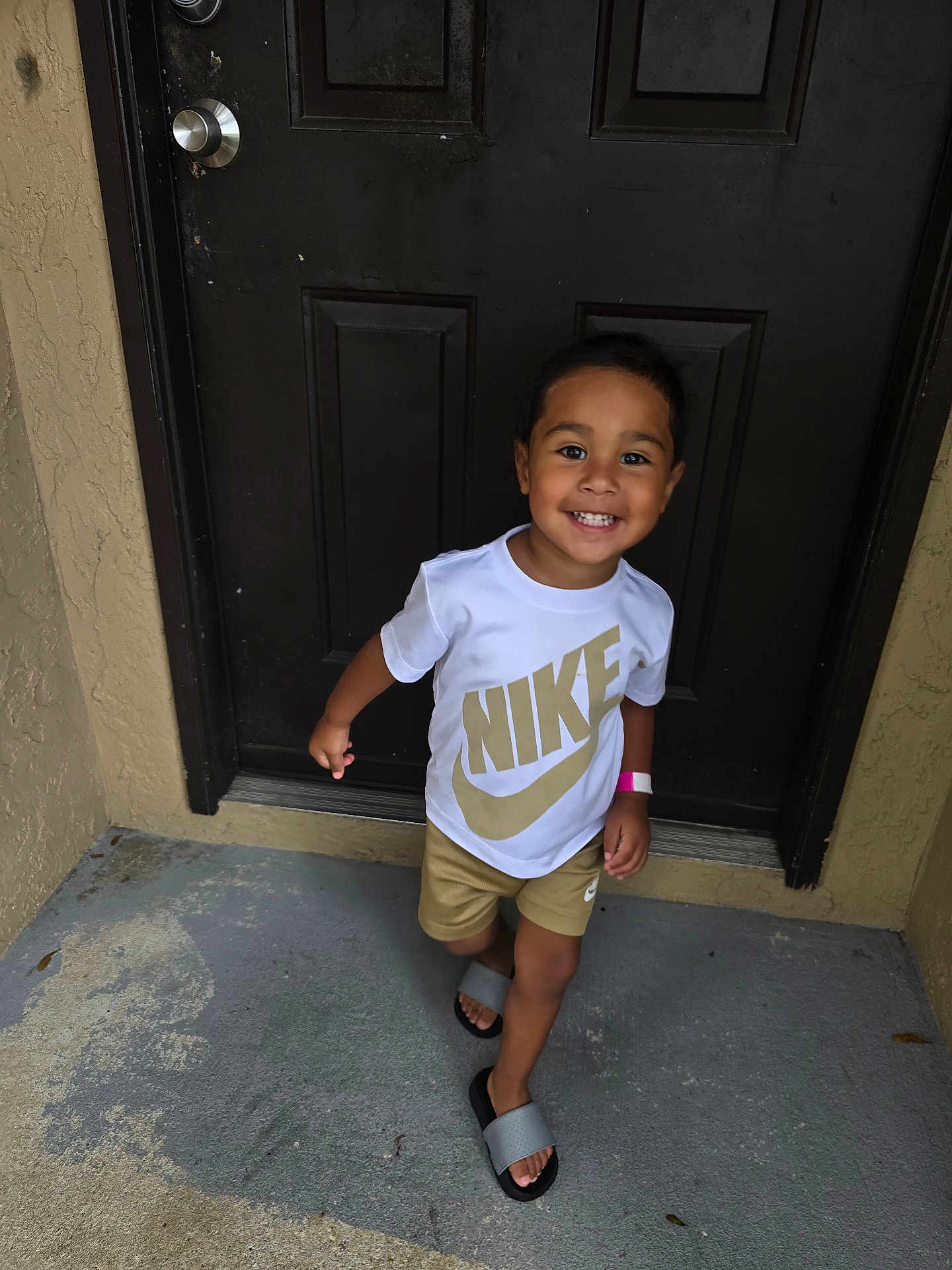 Adriel is registered to the contest to win money with this photo: child, toddler, smile, happy, nike, tshirt, shorts, sandals, door, concrete, outdoor, person, footwear, clothing, walking, young, cute, skin, face, casual