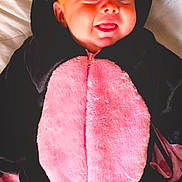 Ivy is registered to the contest to win money with this photo: baby, smiling, onesie, pink, black, cute, infant, happy, face, tongue, bed, soft, cozy, child, costume, sleepwear, lying_down, hood, playful, portrait