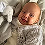 baby, smiling, knitted_sweater, plush_toy, elephant_toy, blanket, cozy, happy, infant, soft_toy, cute, child, portrait, warm, indoors, closeup, person, fabric, comfort, sleepwear