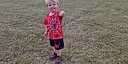 Cody is registered to the contest to win money with this photo: child, boy, grass, field, outdoor, sky, clouds, sailboats, mast, red_clothing, shorts, shoes, smiling, pointing, playful, casual, daylight, nature, young, fun