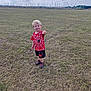 child, boy, grass, field, outdoor, sky, clouds, sailboats, mast, red_clothing, shorts, shoes, smiling, pointing, playful, casual, daylight, nature, young, fun