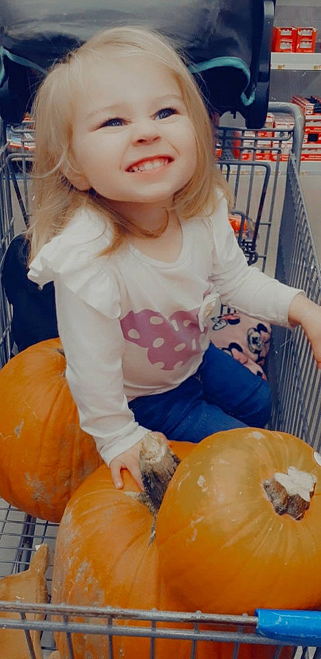 Lyla is registered to the contest to win money with this photo: baby_toddler_clothing, calabaza, cucurbita, facial_expression, gourd, hair, happy, head, joy, natural_foods, organ, person, photograph, plant, pumpkin, shelf, shopping_cart, sleeve, smile, squash