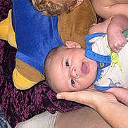 Branson joined the competition — help win amazing prizes! baby, infant, face, hand, blanket, plush_toy, dinosaur_print, onesie, lying_down, curious, happy, human, skin, cute, soft_texture, bedroom, child, person, comfort, indoor