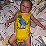 baby, infant, yellow_onesie, dinosaur_print, blanket, animal_pattern, lying_down, cute, child, indoor, soft_toys, pacifier, playmat, young_child, skin, head, arms, legs, expression, comfort
