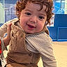 toddler, child, curly_hair, smile, striped_clothing, corduroy, overalls, indoor, blue_wall, ceiling_lights, person, happy, cute, playful, skin, face, hand, floor, modern, portrait