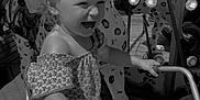 Paolina participe au concours pour gagner de l'argent avec cette photo : child, toddler, motorcycle, carousel, animal_figure, playground, outdoor, smiling, happy, riding, toy, seat, handlebar, clothing, shorts, hair, fun, daylight, amusement_park, black_and_white