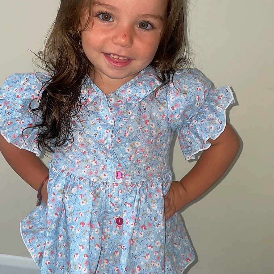 Tildamarie is registered to the contest to win money with this photo: apparel, blue_bow, brown_hair, carpet, casual, child, childhood, cute, fashion, floral_clothing, girl, hands_on_hips, happy, indoor, long_hair, person, portrait, smile, standing, wall