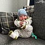 Hugo joined the competition — help win amazing prizes! baby, infant, child, hat, knit_hat, blue_hat, socks, white_socks, green_accents, couch, pillows, plaid_pillows, gray_couch, indoor, holding_foot, pacifier_clip, cozy, cute, smiling, seated