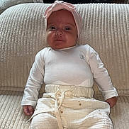 Lya participe au concours pour gagner de l'argent avec cette photo : baby, infant, child, couch, white_clothing, headband, baby_rocker, indoors, cozy, soft_furniture, portrait, smiling, sitting, home, comfortable, cute, young_child, fabric_texture, relaxing, light