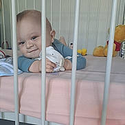 Jules participe au concours pour gagner de l'argent avec cette photo : baby, bars, bed, blue_clothing, child, crib, cute, face, indoor, infant, lying_down, person, pink_sheet, playful, plush_toy, room, smile, soft_toy, toy, winnie_the_pooh