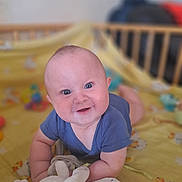 Jules a rejoint le concours — aidez-le/la à gagner de superbes lots ! baby, blanket, blue_eyes, child, closeup, crawling, crib, cute, cute_expression, face, happy, indoors, infant, person, plush_toy, short_hair, smiling, soft_toy, toddler, yellow_blanket
