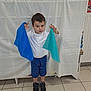 background_sheet, black_shoes, blue_cloth, blue_shorts, boy, casual_clothing, child, cloth, fabric, floor_tiles, indoor, neutral_expression, person, portrait, short_hair, standing, teal_cloth, tile_floor, white_shirt, young_child