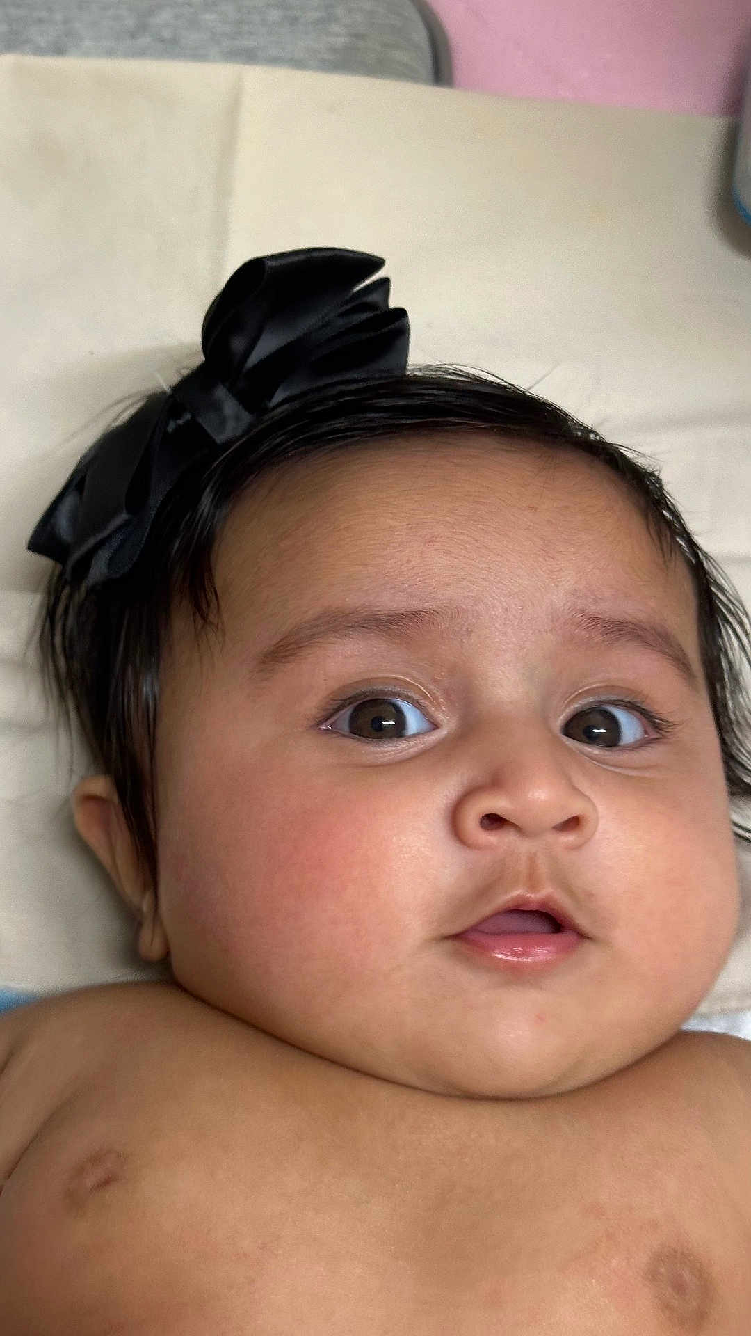 Aanvi joined the competition — help win amazing prizes! baby, infant, face, head, black_bow, wide_eyes, curious, skin, cheeks, mouth, expression, lying_down, soft_surface, indoors, closeup, child, person, cute, adorable, portrait