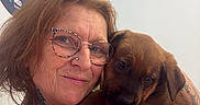 Louky participe au concours pour gagner de l'argent avec cette photo : woman, glasses, tattoos, puppy, dog, pet, indoor, smile, person, holding, brown_dog, cute, affection, face, portrait, casual_clothing, light_blue_wall, sign, friendly, animal
