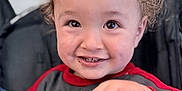 Luka is registered to the contest to win money with this photo: toddler, child, smiling, curly_hair, hand, cookie, clothing, red_sleeves, face, eyes, teeth, indoor, seat, stroller, happy, portrait, baby, person, cute, expression