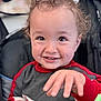 Luka is registered to the contest to win money with this photo: toddler, child, smiling, curly_hair, hand, cookie, clothing, red_sleeves, face, eyes, teeth, indoor, seat, stroller, happy, portrait, baby, person, cute, expression