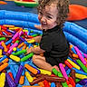 Luka joined the competition — help win amazing prizes! toddler, child, curly_hair, black_clothing, blue_inflatable_pool, colorful_toys, soft_toys, play_area, smiling, happy, indoor, playtime, bright_colors, fun, cute, person, baby, plastic_toys, sitting, portrait