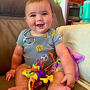 Callum joined the competition — help win amazing prizes! baby, smiling, sitting, toy, onesie, couch, indoor, home, furniture, child, happy, foot, hand, face, living_room, colorful, blanket, kitchen, cup, playful