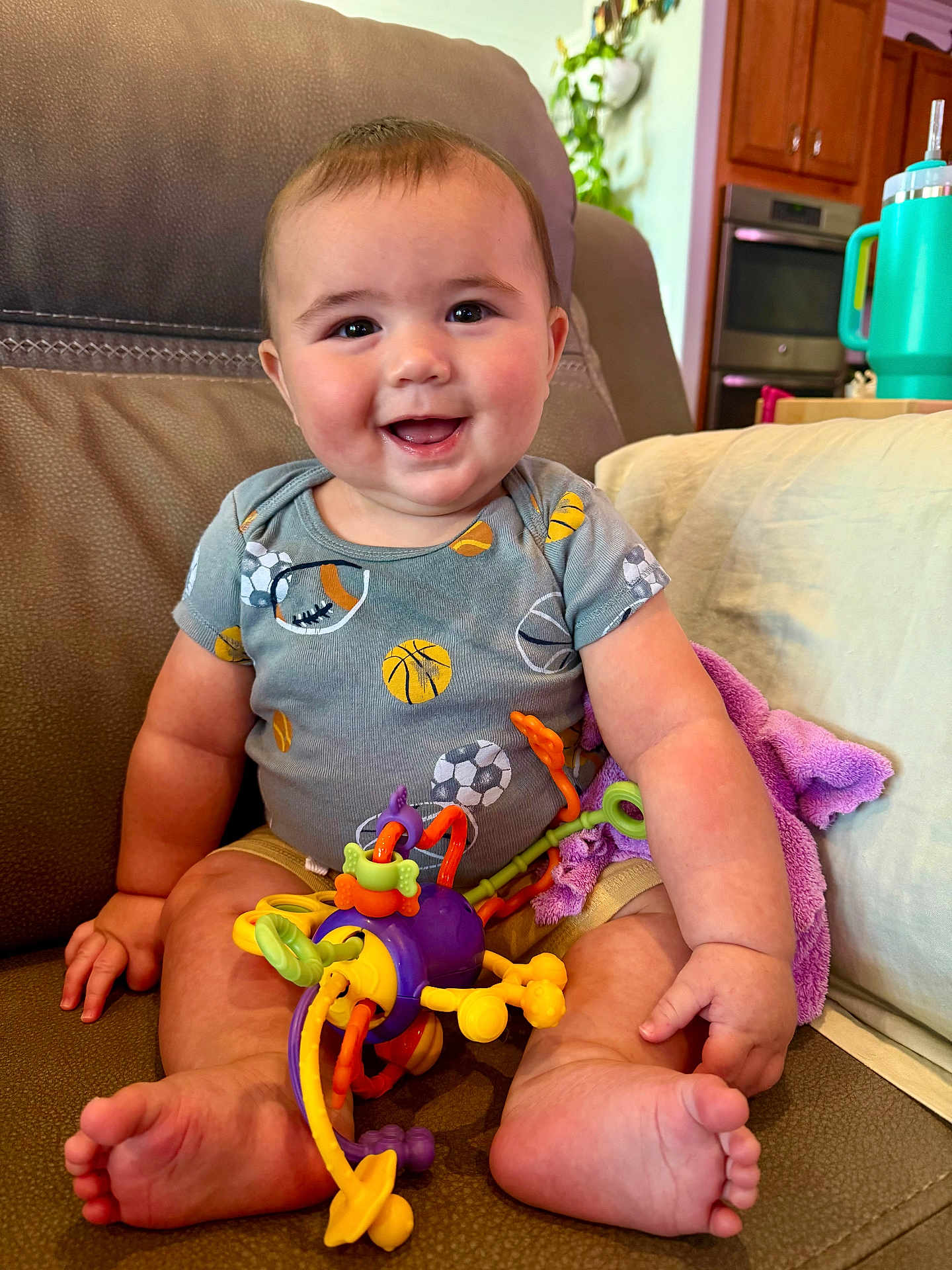 Callum joined the competition — help win amazing prizes! baby, smiling, sitting, toy, onesie, couch, indoor, home, furniture, child, happy, foot, hand, face, living_room, colorful, blanket, kitchen, cup, playful