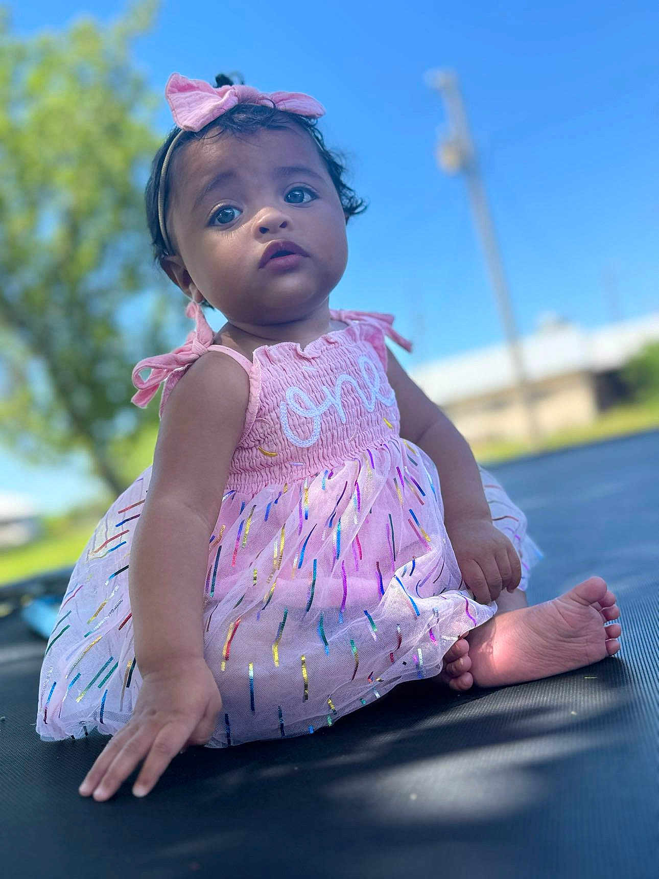 Aniyah joined the competition — help win amazing prizes! toddler, child, outdoor, dress, pink, headband, baby, sitting, face, portrait, curious, trampoline, sunlight, nature, grass, blue_sky, smile, cute, young_child, colorful