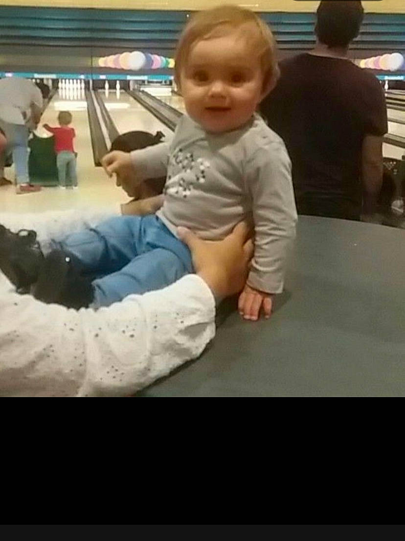 Sarah participe au concours pour gagner de l'argent avec cette photo : arm, baby, clothing, comfort, face, finger, floor, flooring, fun, hairstyle, head, human_body, person, skin, sleeve, standing, t_shirt, table, ten_pin_bowling, toddler