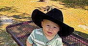 Rhett joined the competition — help win amazing prizes! baby, child, cowboy_hat, face, grass, nature, outdoor, park, patterned_pants, person, picnic_table, playful, portrait, seated, shadows, smiling, striped_shirt, stump, sunlight, trees