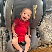Rhett is registered to the contest to win money with this photo: baby, camouflage, car_seat, child, comfortable, couch, face, floor, footwear, furniture, happy, indoor, infant, patterned, person, red_onesie, seat, shoe, smiling, wooden_floor