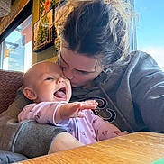 Amelia is registered to the contest to win money with this photo: baby, woman, mother, child, kiss, love, hug, indoor, cafe, window, natural_light, joy, happy, sweatshirt, table, person, face, skin, hair, clothing