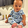Osiah is registered to the contest to win money with this photo: baby, child, pajamas, blue_clothing, smile, sitting, barefoot, face, cute, indoor, table, curtain, floor, person, infant, hand, foot, expression, young_child, portrait