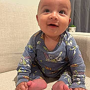 Osiah is registered to the contest to win money with this photo: baby, child, smiling, blue_onesie, cartoon_characters, sitting, couch, beige, happy, indoors, feet, hands, head, face, curtain, potted_plant, cozy, cute, portrait, infant