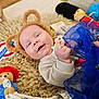 baby, smiling, bear_ears, fluffy_rug, toy, stuffed_animal, blue_fabric, hand_holding, indoor, child, cute, happy, infant, blanket, playtime, colorful, soft_texture, person, face, lying_down