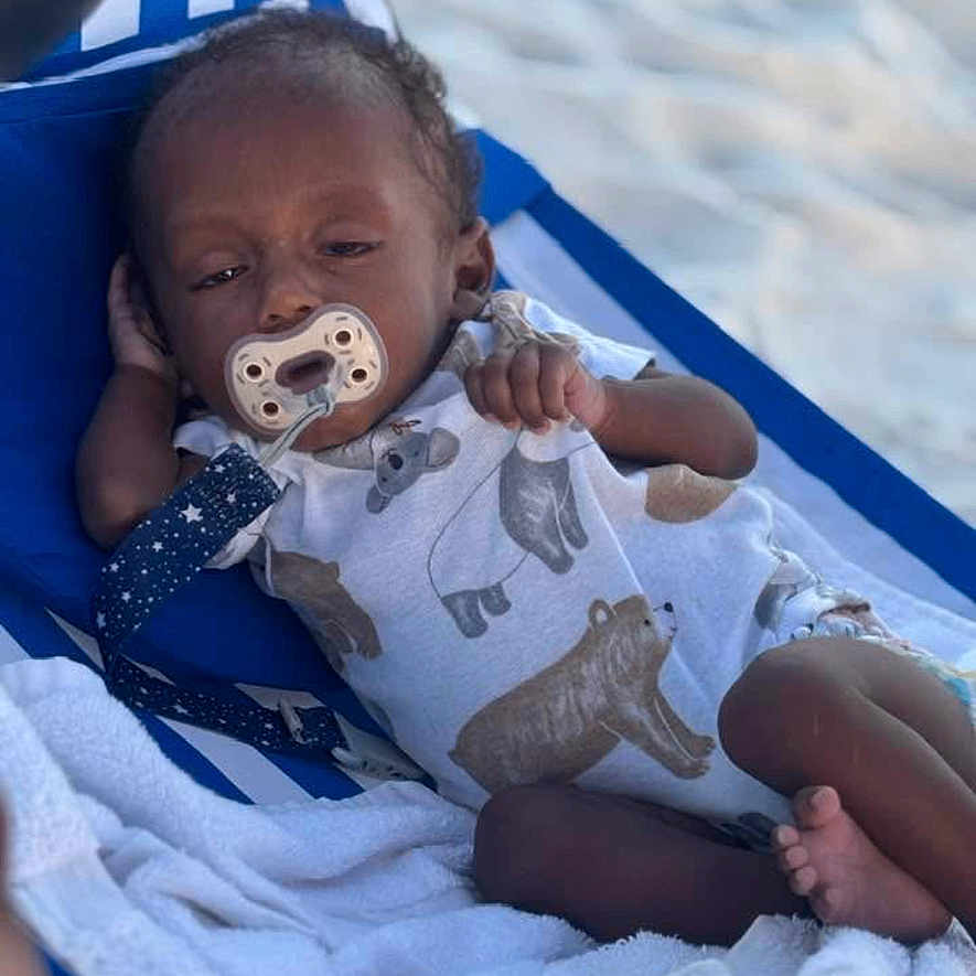 Kelvin is registered to the contest to win money with this photo: animal_print, baby, beach_chair, child, clothing, comfort, cute, infant, onesie, outdoor, pacifier, person, relaxing, resting, sand, sleepy, striped, summer, towel, vacation