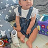 Aria is registered to the contest to win money with this photo: baby, child, toddler, denim_overalls, white_top, headband, indoor, toys, colorful, cushions, playmat, footwear, sitting, cute, face, person, infant, playroom, soft_toys, expression