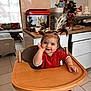 baby, child, high_chair, red_clothing, reindeer_antlers, pigtails, kitchen, christmas_tree, holiday_decorations, smile, festive, indoor, wooden_furniture, cute, happy, person, face, table, tile_floor, home