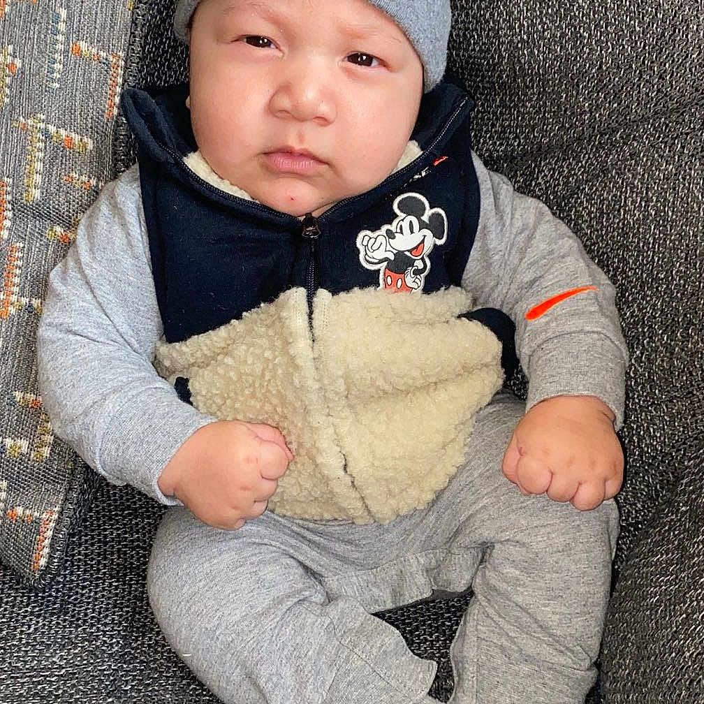 Kairo is registered to the contest to win money with this photo: baby, bonnet, cap, clothing, coat, couch, face, furniture, hat, head, hosiery, jacket, knitwear, pants, person, photography, portrait, sleeping, sock, sweater