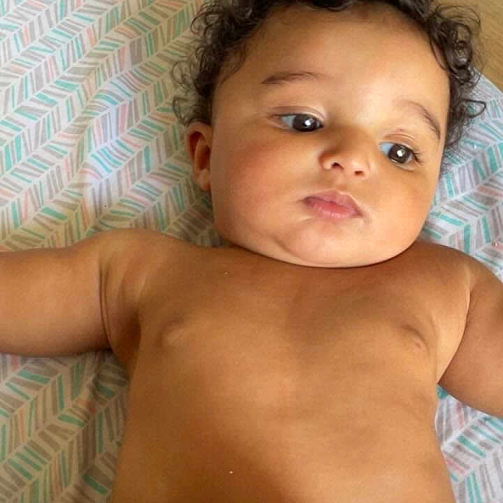 Cameron is registered to the contest to win money with this photo: baby, child, curly_hair, blanket, pattern, floor, indoor, portrait, cute, skin, lying_down, infant, expression, head, face, diaper, soft, cozy, home, relaxed
