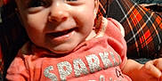 Maya is registered to the contest to win money with this photo: baby, child, smiling, pink_shirt, text_on_clothing, plaid_blanket, happy, indoor, face, person, cute, young_child, sitting, blue_eyes, short_hair, clothing, infant, portrait, casual, closeup