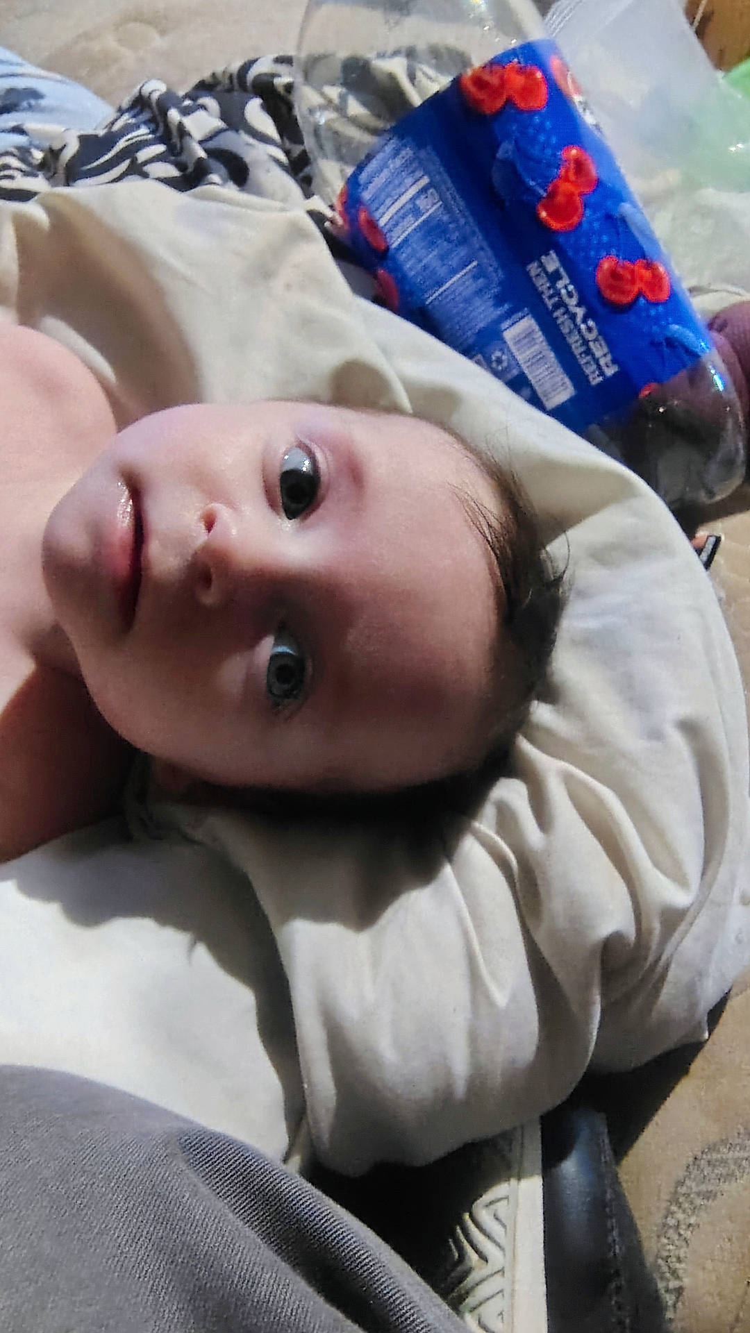 Maya is registered to the contest to win money with this photo: baby, blanket, bottle, casual, child, clothing, curious, expression, face, hair, head, home, indoor, lying_down, pillow, plastic, portrait, skin, soda, soft