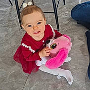 April a rejoint le concours — aidez-le/la à gagner de superbes lots ! toddler, child, smiling, red_dress, white_tights, stuffed_animal, pink, toy, indoor, floor, tile_floor, bow, happy, person, cute, sitting, blue_eyes, playful, furniture_legs, home