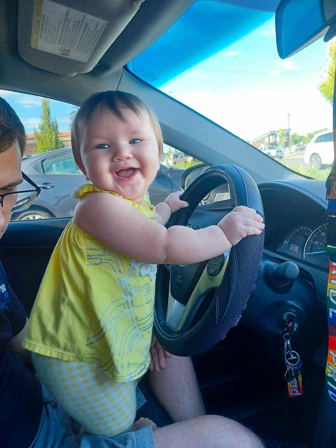 Bobbie is registered to the contest to win money with this photo: auto_part, automotive_design, automotive_exterior, automotive_mirror, car, car_seat, car_seat_cover, finger, joy, mode_of_transport, motor_vehicle, person, product, sky, smile, steering_part, steering_wheel, summer, thumb, toddler