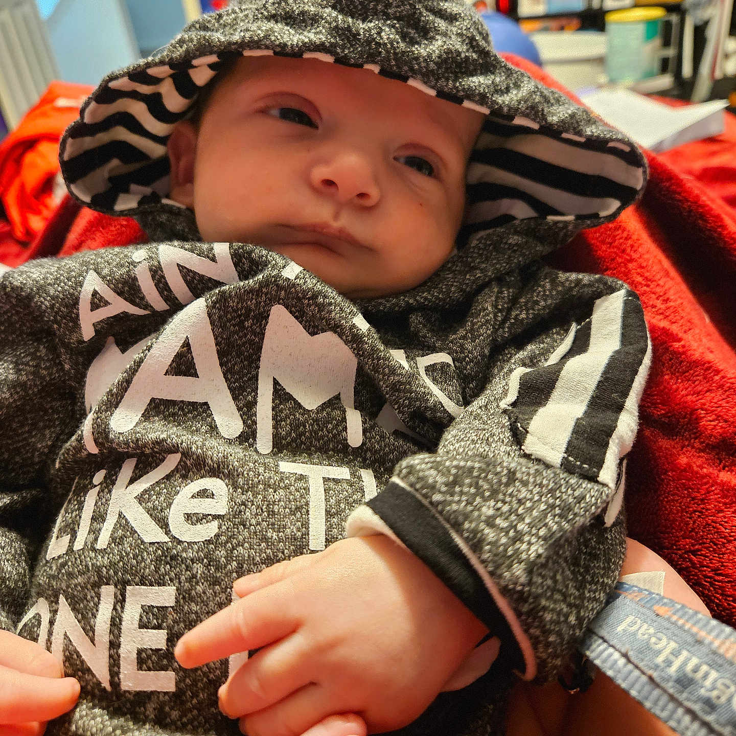 Ezekiel Edward joined the competition — help win amazing prizes! baby, blanket, clothing, cozy, cute, expression, face, foot, hand, hood, indoor, infant, person, portrait, red, relaxed, small, striped, sweater, warm