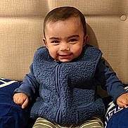 Arham Islam is registered to the contest to win money with this photo: baby, child, smile, blue_vest, striped_pants, booties, pillow, couch, patterned_blanket, indoor, headboard, happy, seated, cozy_clothing, portrait, infant, cute, home_interior, fabric_texture, comfortable