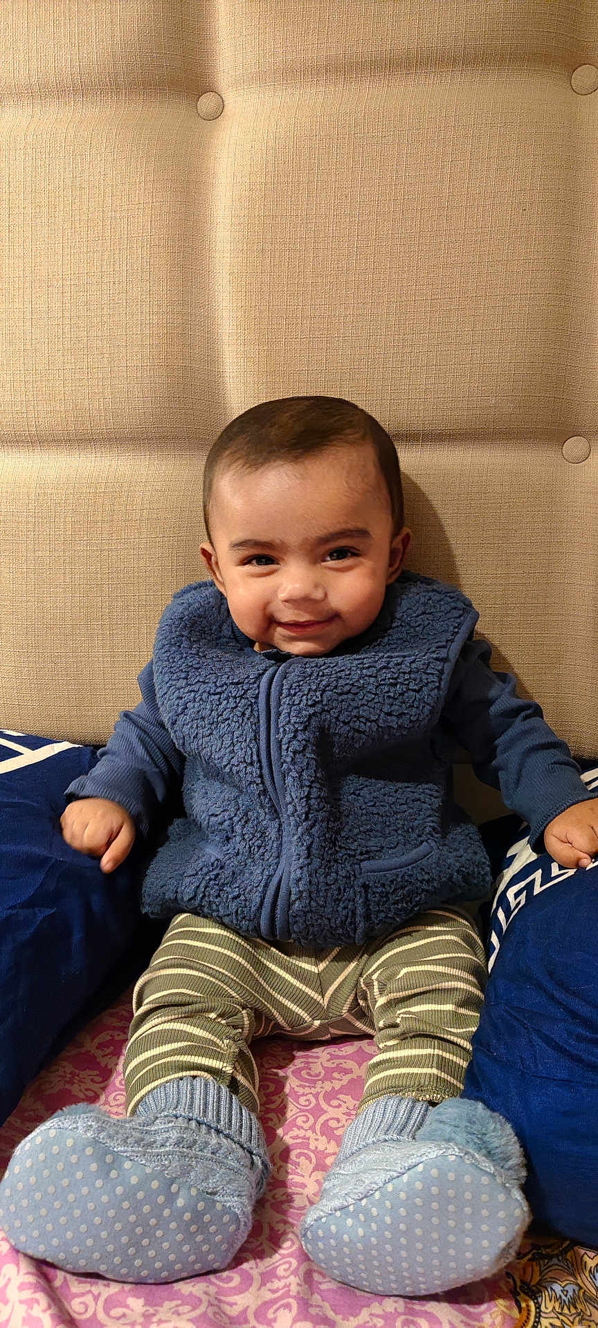 Arham Islam is registered to the contest to win money with this photo: baby, child, smile, blue_vest, striped_pants, booties, pillow, couch, patterned_blanket, indoor, headboard, happy, seated, cozy_clothing, portrait, infant, cute, home_interior, fabric_texture, comfortable