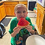 child, boy, watermelon, kitchen, green_shirt, smiling, food, fruit, tile_floor, cabinet, stove, table, plate, happy, indoor, person, cute, eating, home, backpack