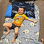 John is registered to the contest to win money with this photo: child, boy, smiling, pajamas, blanket, polar_bear, pillow, dinosaur, indoor, carpet, floor, yellow_shirt, shorts, happy, cute, relaxed, home, casual, playful, comfort